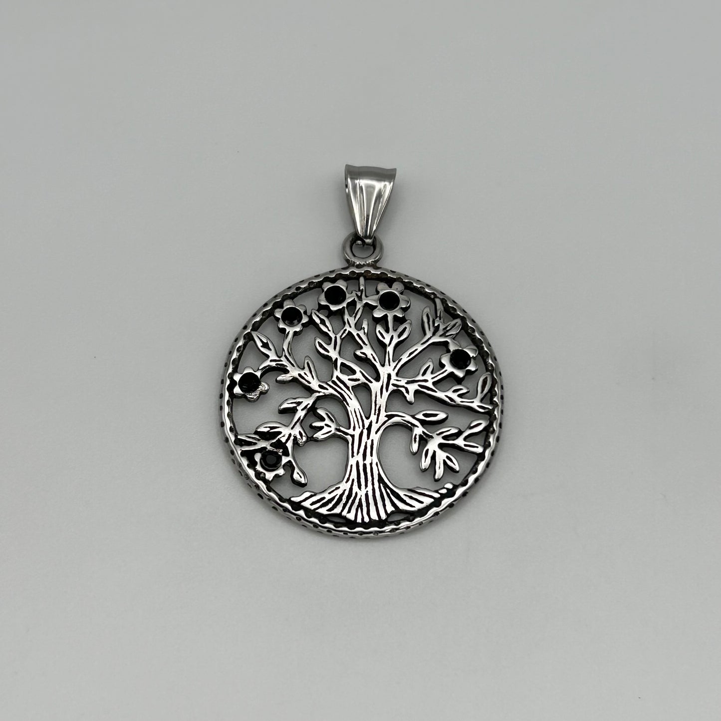 A silver stainless steel pendant in the shape of a tree with a circular frame, attached to a small circular chain.