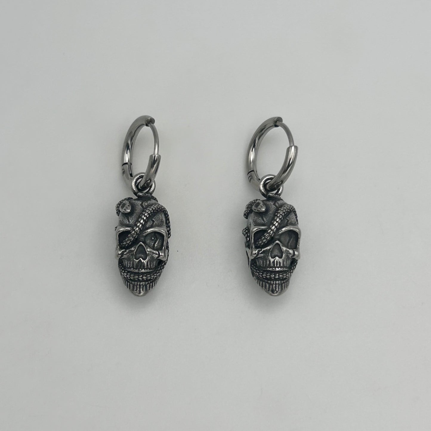 A pair of stainless steel Huggie earrings with a skull design.